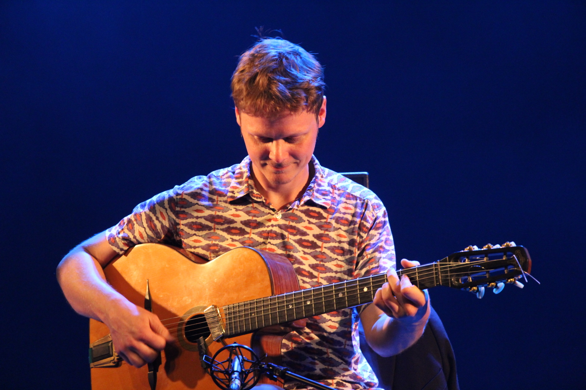 Jean Guyomarc’h joue de la guitare sur scène sous des lumières bleues et ambrées